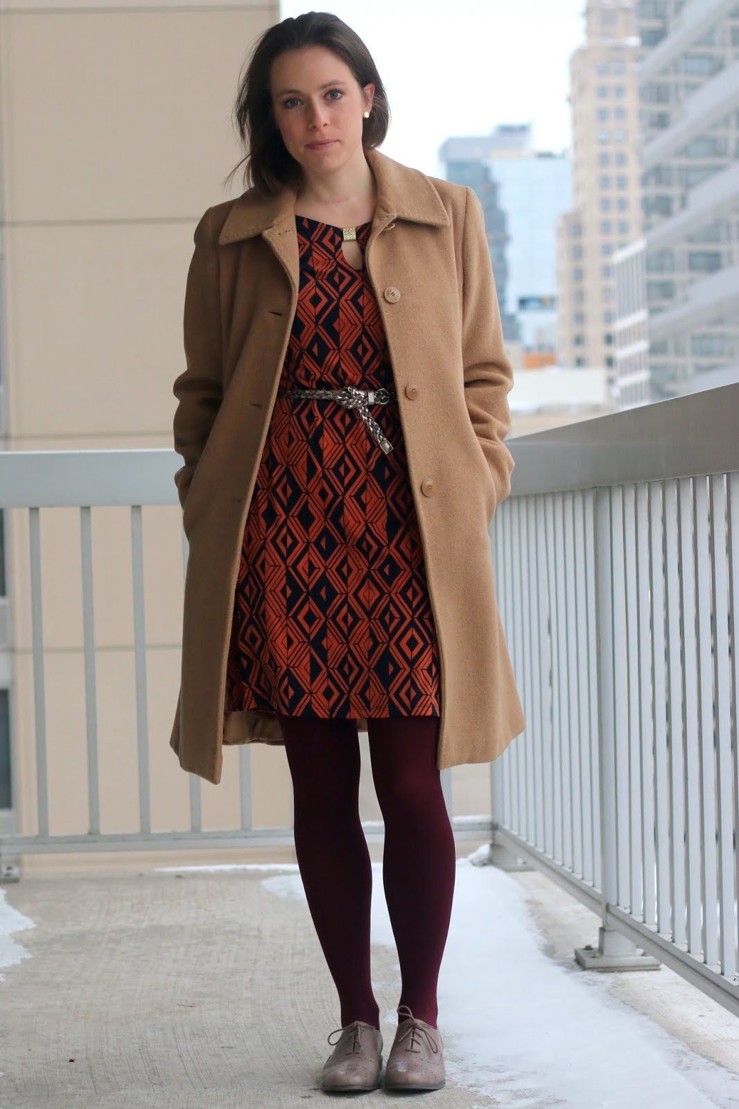 FashionablyEmployed.com | Orange and Navy geometric pattern dress, burgundy tights, gray belt and oxfords, camel winter coat | wear to work outfit, office style | versatile wardrobe workhorses