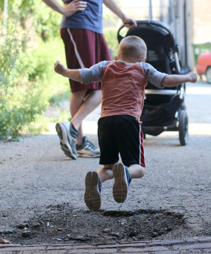 little boy jumping over a pothole in the city