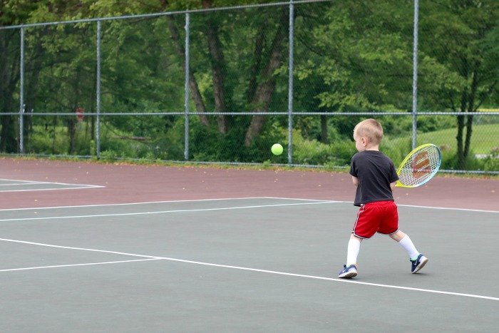 little boy hitting tennis ball on tennis court