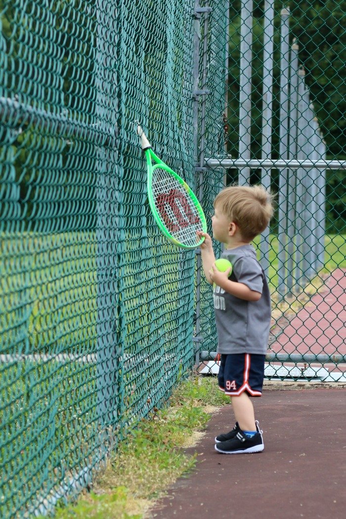 little boy sticking tennis racquet through fence