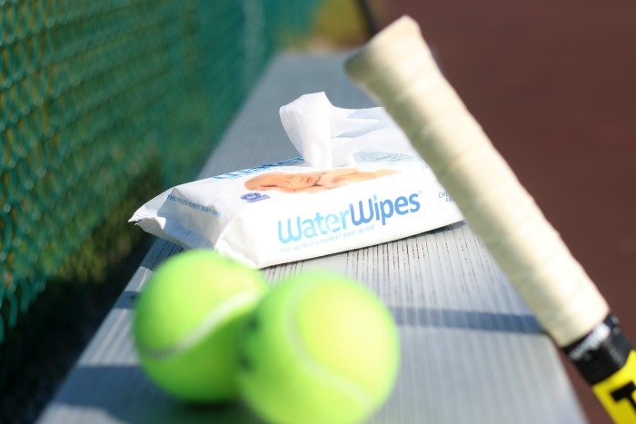 water wipes on a tennis court bench with a racquet and balls