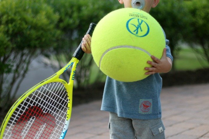 little boy holding oversize tennis ball and racket in burts bees kids clothes