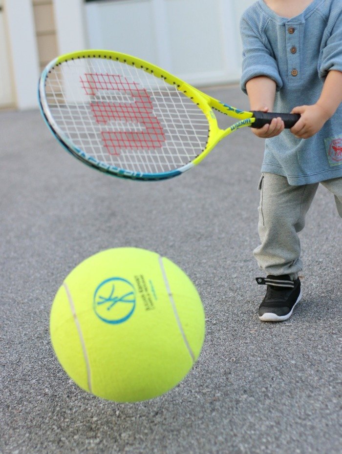little boy playing tennis with oversize tennis ball and racket