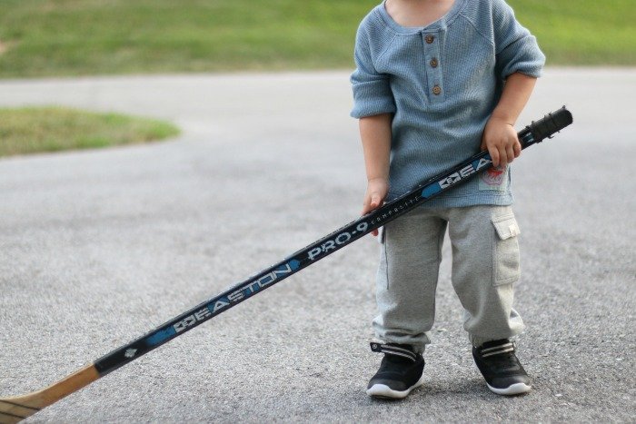 little boy with a large hockey stick playing sports in the driveway