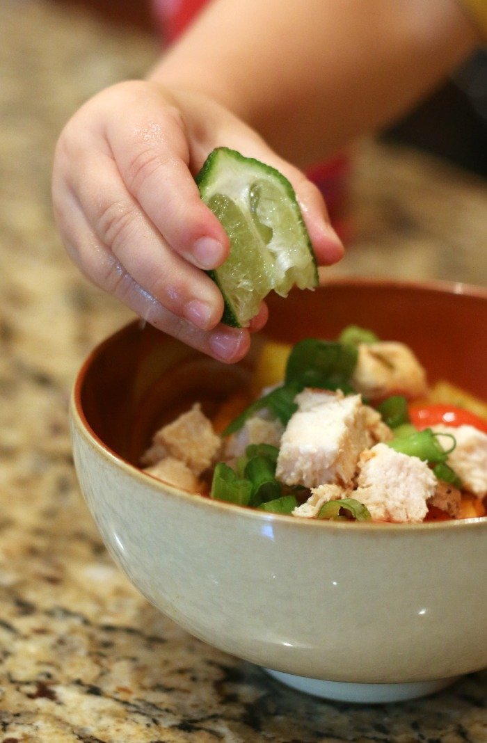 little boy hand squeezing a lime onto a bowl of chicken and chopped vegetables