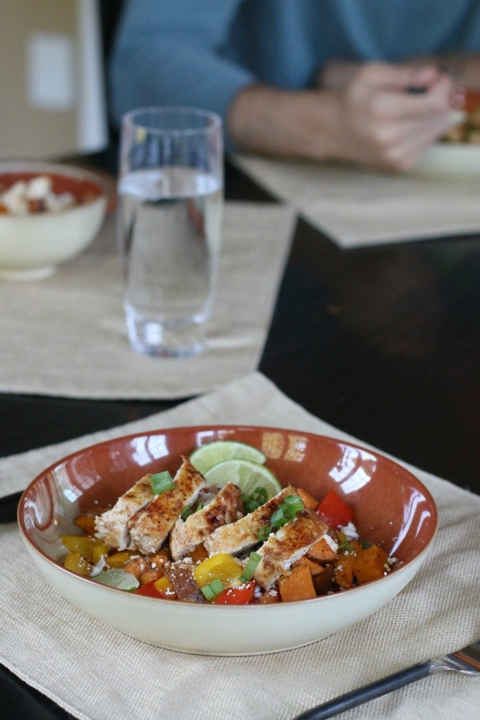 southwestern spiced chicken with peppers sweet potatos and lime wedges in a bowl served for dinner with arm in background