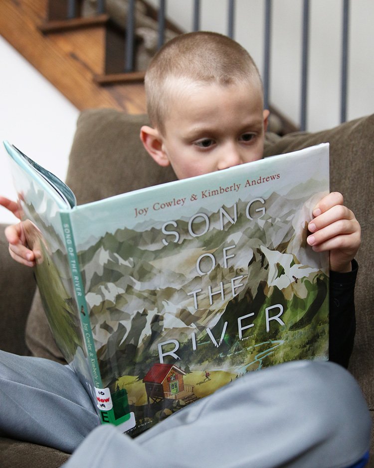 young boy reading a picture book called Song of the River, a great picture book for Earth Day