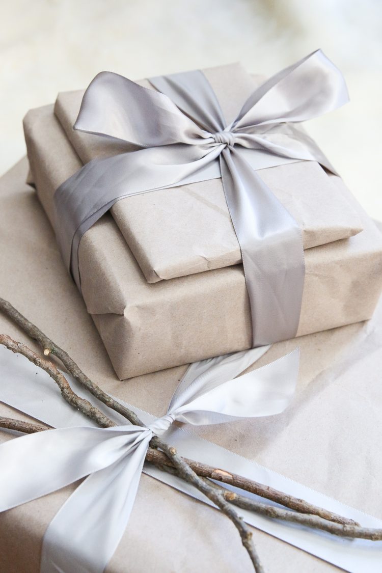 pile of gifts wrapped in brown paper with silver ribbon and two twigs as a decoration on the package