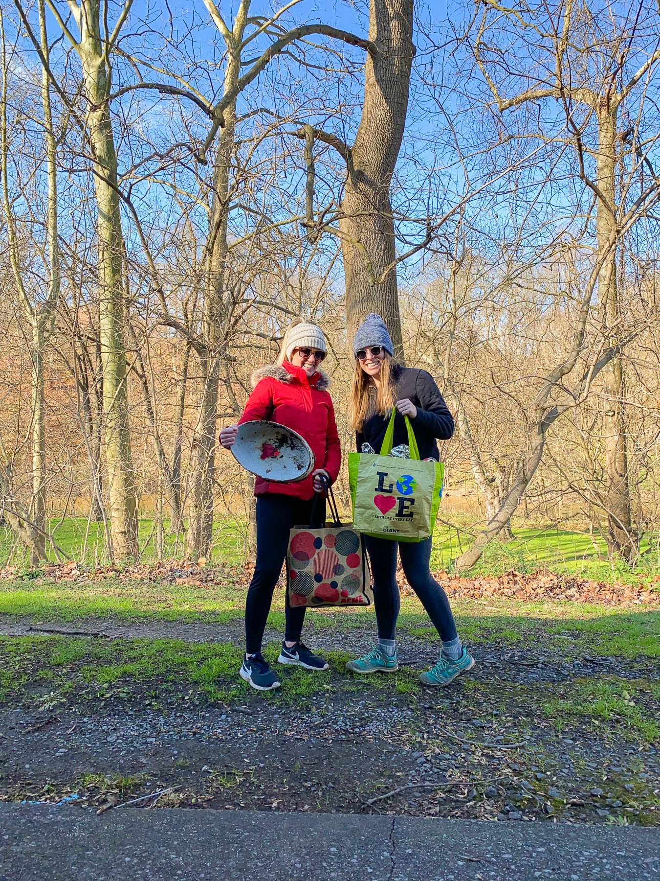 two women holding litter pick up items in the woods