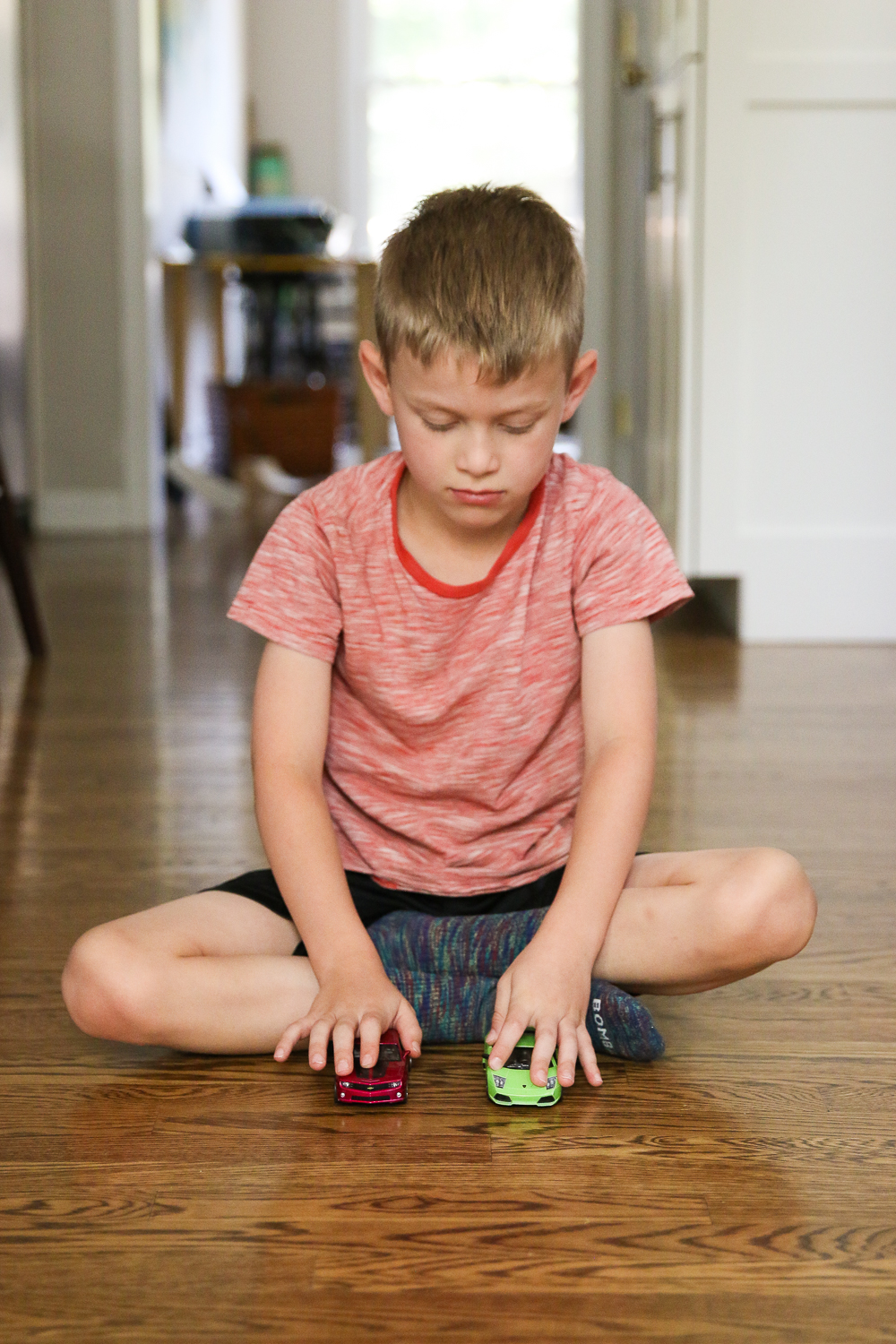 Boy sitting on hardwood floor playing with two toy cars