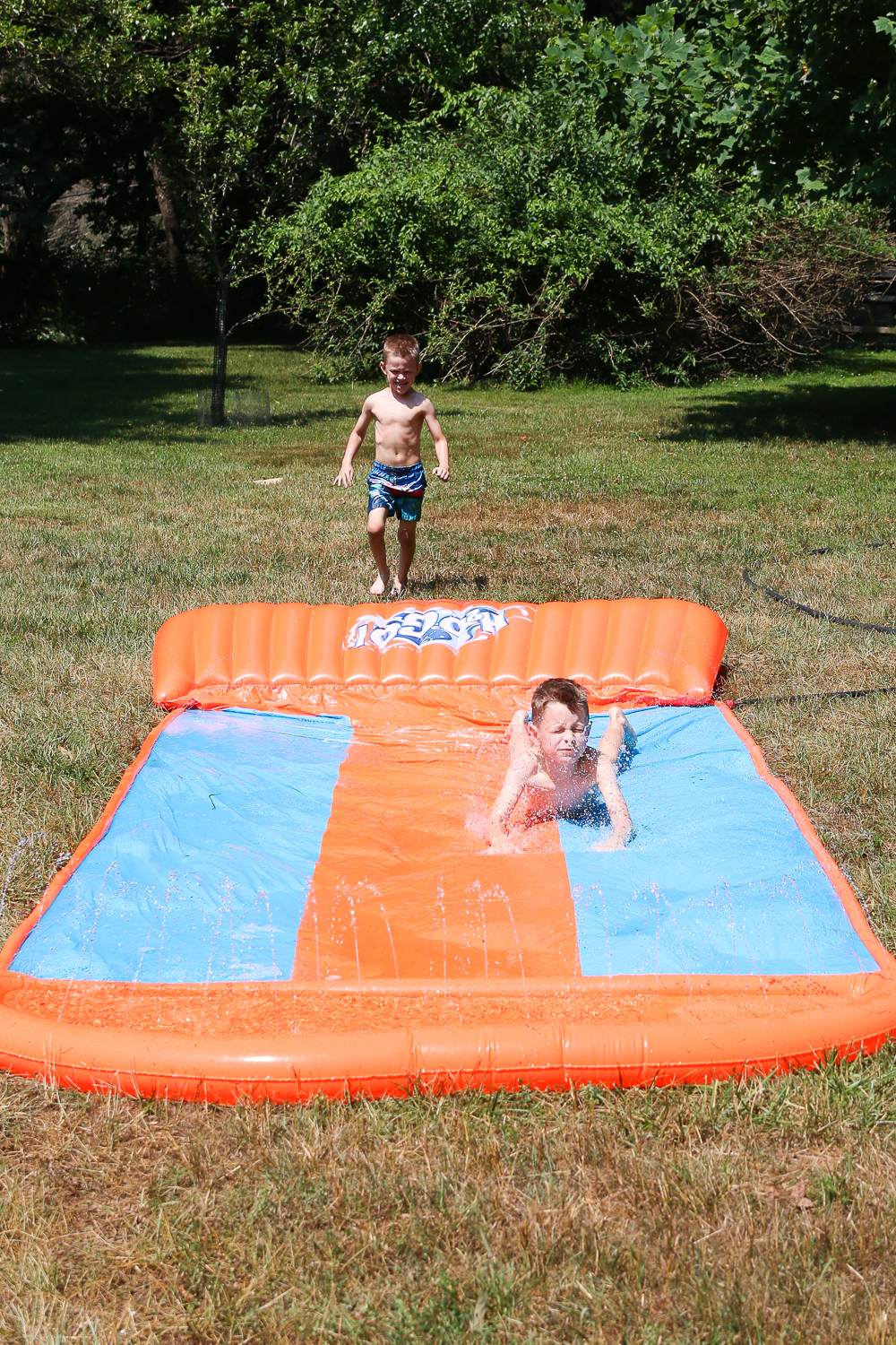 Two boys playing outside on a plastic slip and slide/ splash pad