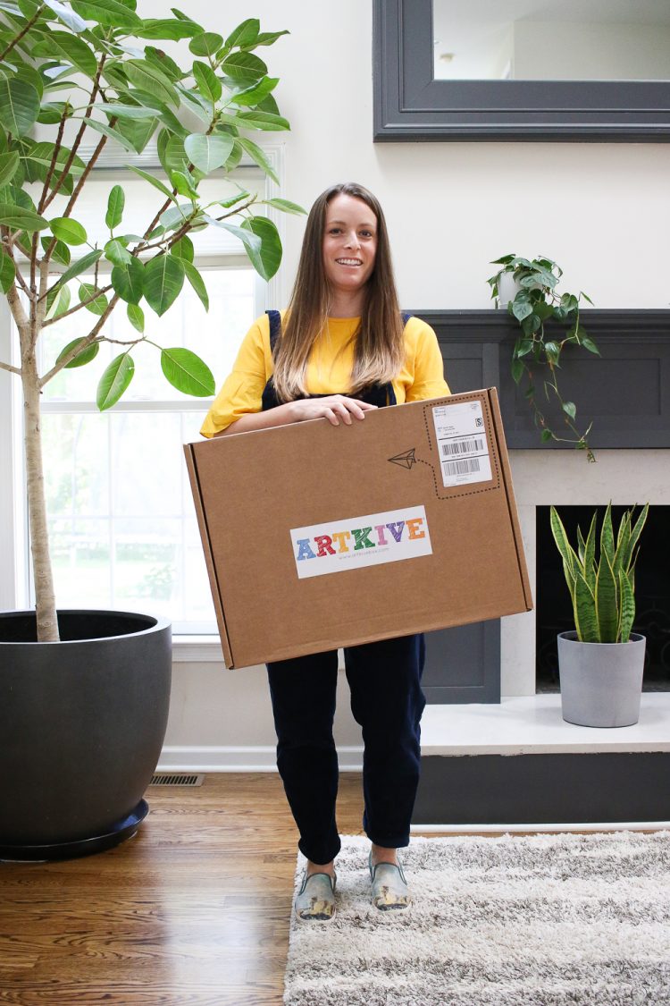 Jen standing and holding the large cardboard box from artkive with kids art inside