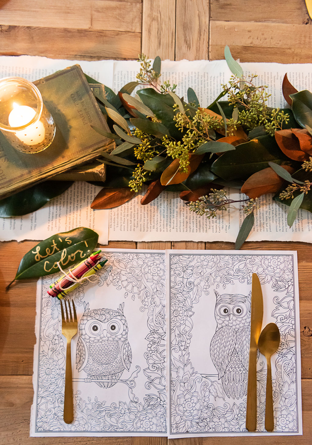place setting with floral garland, silverware, and kids coloring pages as placemats with a bundle of crayons sitting on a table