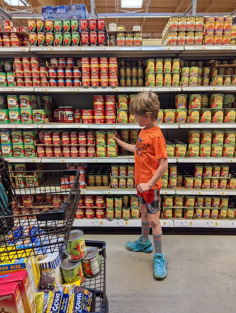 boy grabbing can of tomato sauce from grocery shelf