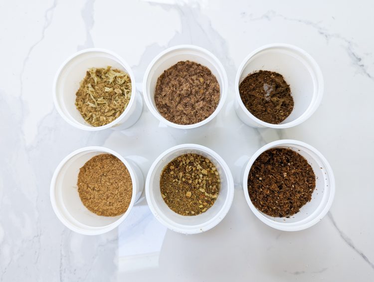 image of six plastic containers, each with one batch of output from an electric composter - none of which look like finished compost