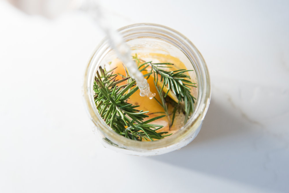 pouring distilled vinegar into a mason jar with rosemary and grapefruit peels